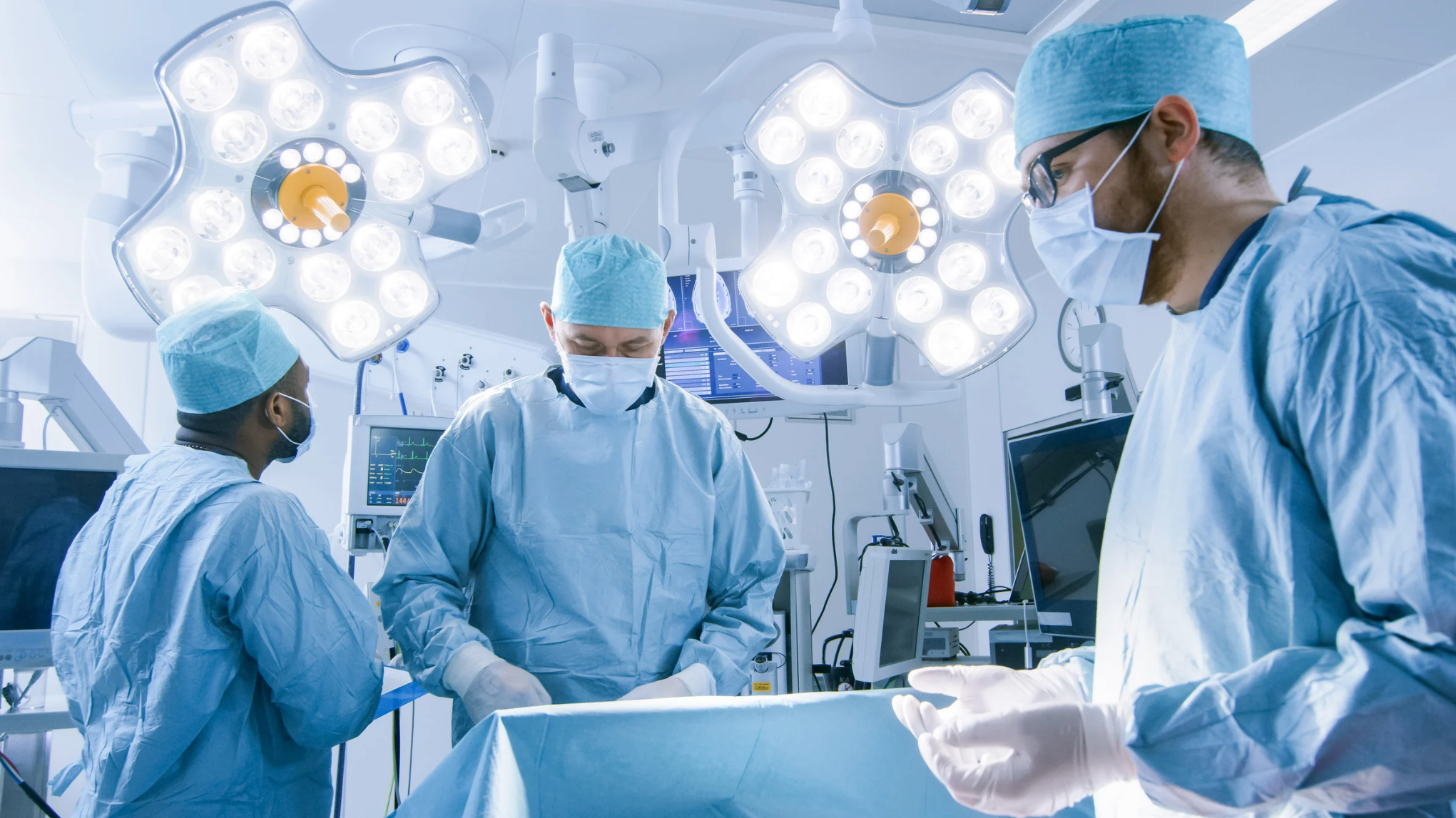 Surgeons in an operating room with medical equipment and lights.
